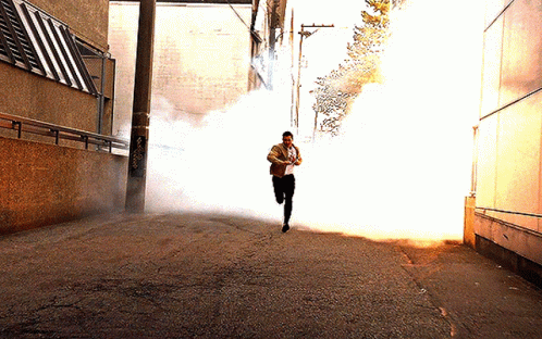 A Man Is Running Through A Smokey Alleyway GIF