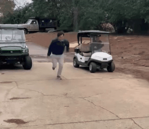 A Man Is Running Towards A Golf Cart That Is Parked In A Driveway GIF