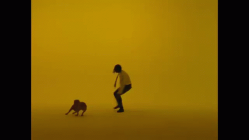 A Man Is Running With A Dog In Front Of A Yellow Wall GIF
