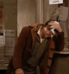 A Man Is Scratching His Head While Sitting At A Counter In A Store . GIF