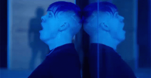 A Man Is Screaming In Front Of A Mirror And His Reflection Is Visible . GIF