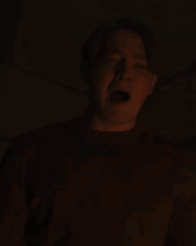 A Man Is Screaming In The Dark With His Mouth Open And His Tongue Sticking Out GIF