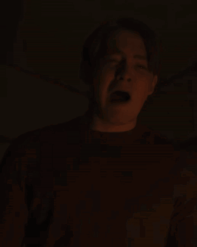 A Man Is Screaming In The Dark With His Mouth Open And His Tongue Sticking Out GIF