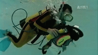 A Man Is Scuba Diving In A Pool With A Camera . GIF