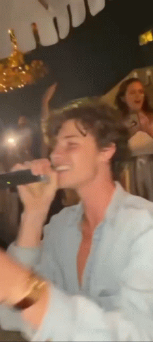A Man Is Singing Into A Microphone At A Party In A Dark Room . GIF