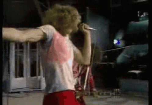 A Man Is Singing Into A Microphone In A Dark Room GIF
