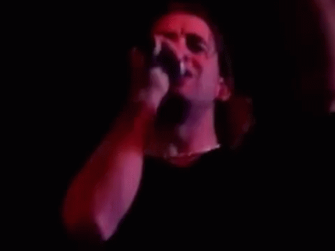 A Man Is Singing Into A Microphone In A Dark Room With Red Lights . GIF