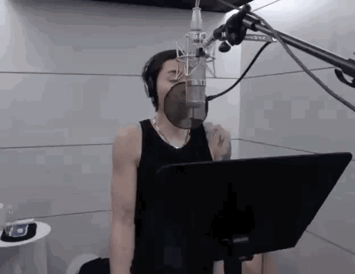 A Man Is Singing Into A Microphone In A Recording Studio While Wearing Headphones . GIF