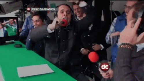 A Man Is Singing Into A Microphone In Front Of A Green Screen That Says Dc GIF