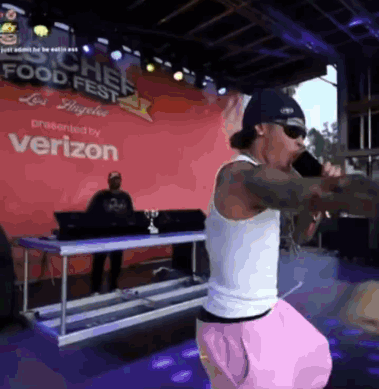 A Man Is Singing Into A Microphone In Front Of A Verizon Sign GIF