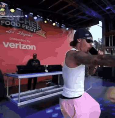 A Man Is Singing Into A Microphone In Front Of A Verizon Sign GIF