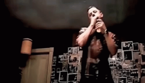 A Man Is Singing Into A Microphone In Front Of A Wall Covered In Pictures . GIF