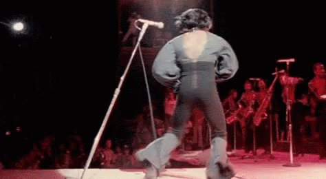 A Man Is Singing Into A Microphone On A Stage . GIF