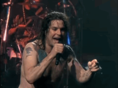 A Man Is Singing Into A Microphone On A Stage GIF