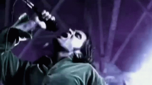 A Man Is Singing Into A Microphone On A Stage In A Dark Room . GIF
