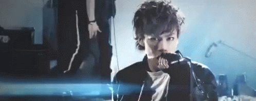 A Man Is Singing Into A Microphone On A Stage In Front Of A Crowd . GIF