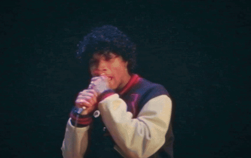 A Man Is Singing Into A Microphone On A Stage In Front Of A Crowd . GIF