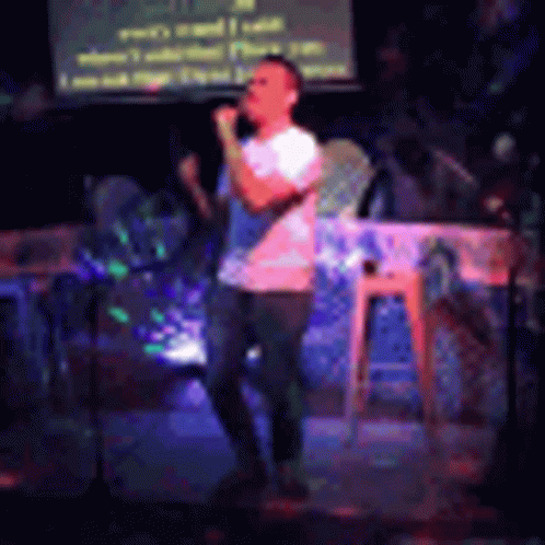 a man is singing into a microphone on a stage in front of a screen .