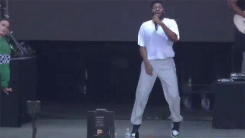 A Man Is Singing Into A Microphone On A Stage While Dancing . GIF
