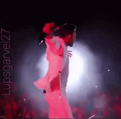 A Man Is Singing Into A Microphone On A Stage With A Crowd Behind Him . GIF