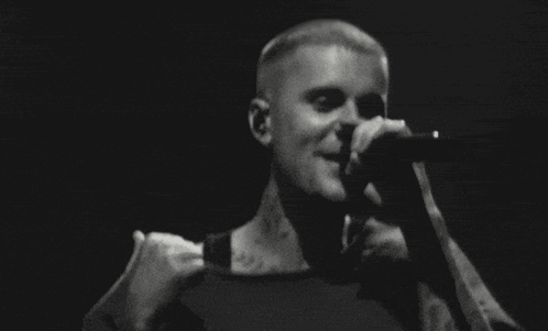 A Man Is Singing Into A Microphone On Stage In A Black And White Photo . GIF