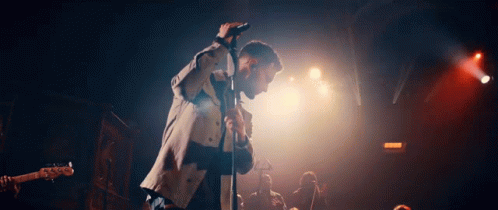 A Man Is Singing Into A Microphone On Stage In Front Of A Crowd GIF