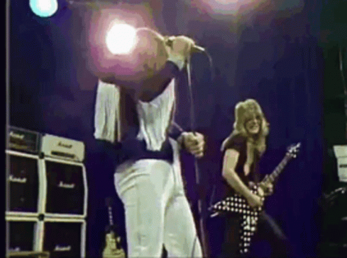 A Man Is Singing Into A Microphone While Another Man Plays A Guitar On Stage . GIF