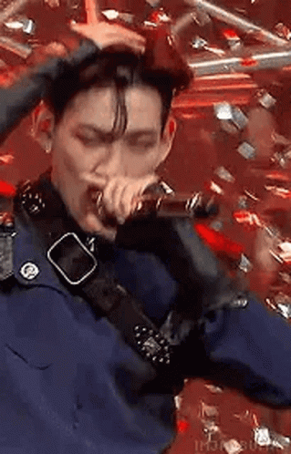 A Man Is Singing Into A Microphone While Holding His Hair . GIF