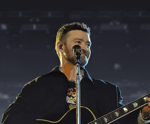 A Man Is Singing Into A Microphone While Playing A Guitar GIF