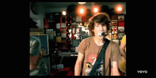 a man is singing into a microphone while playing a guitar in a room with records on the wall .
