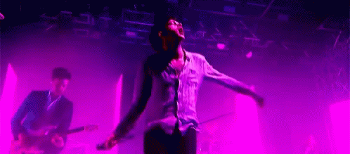 A Man Is Singing Into A Microphone While Playing A Guitar On Stage . GIF