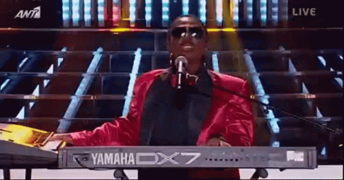 A Man Is Singing Into A Microphone While Playing A Yamaha Dx7 Keyboard . GIF
