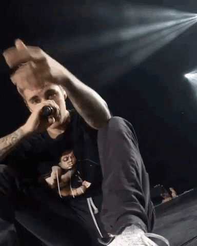 A Man Is Singing Into A Microphone While Sitting On A Stage GIF