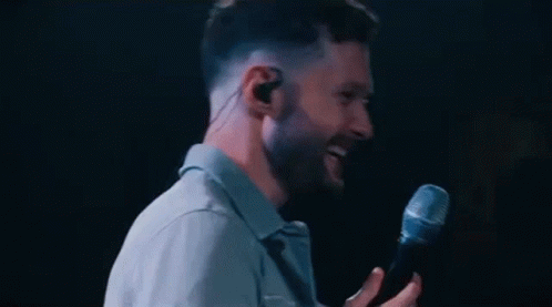 A Man Is Singing Into A Microphone While Wearing Earbuds . GIF