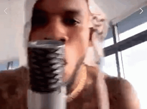 A Man Is Singing Into A Microphone With A Window Behind Him GIF