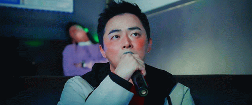 A Man Is Singing Into A Microphone With His Hand On His Chin GIF