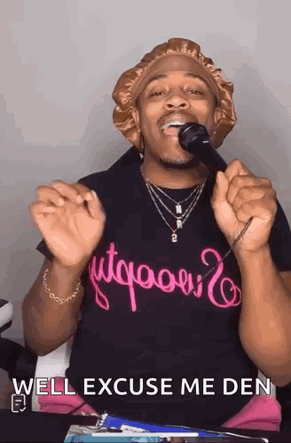 A Man Is Singing Into A Microphone With The Words `` Well Excuse Me Den '' Written On His Shirt . GIF