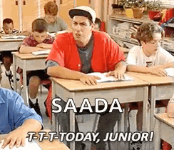 A Man Is Sitting At A Desk In A Classroom With Other Students . GIF