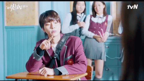 A Man Is Sitting At A Desk In A Classroom With Two Girls Standing Behind Him And A Tvn Logo In The Corner GIF