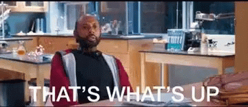 A Man Is Sitting At A Desk In A Kitchen With The Words `` That 'S What 'S Up '' Written Above Him . GIF