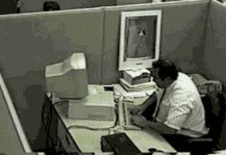 A Man Is Sitting At A Desk In An Office Cubicle With A Computer . GIF