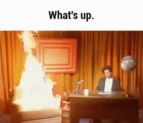 A Man Is Sitting At A Desk In Front Of A Fire And The Words What 'S Up . GIF