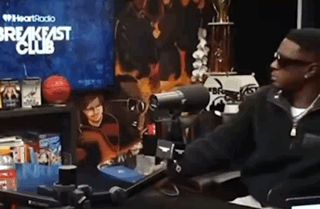 a man is sitting at a desk in front of a microphone in front of a breakfast club sign .
