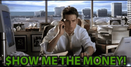 A Man Is Sitting At A Desk Talking On A Cell Phone With The Words Show Me The Money Written Below Him GIF