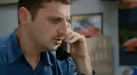 A Man Is Sitting At A Desk Talking On A Cell Phone . GIF