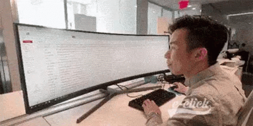 A Man Is Sitting At A Desk Using A Computer With A Large Screen . GIF