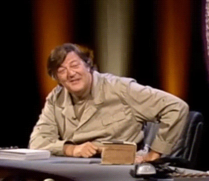 A Man Is Sitting At A Desk With A Book And A Phone On It . GIF