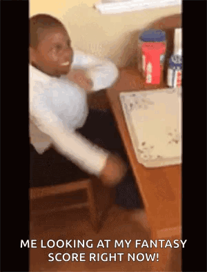 A Man Is Sitting At A Desk With His Arms Outstretched And Looking At His Fantasy Score Right Now . GIF