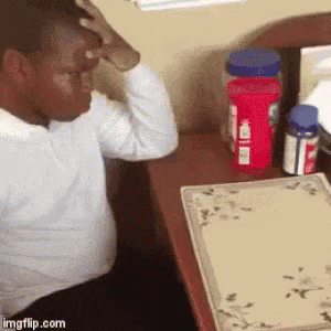 A Man Is Sitting At A Desk With His Hand On His Head And Bottles Of Medicine On The Table . GIF