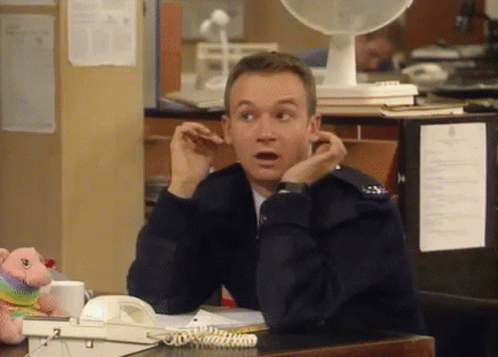 A Man Is Sitting At A Desk With His Hands On His Ears And A Fan Behind Him . GIF